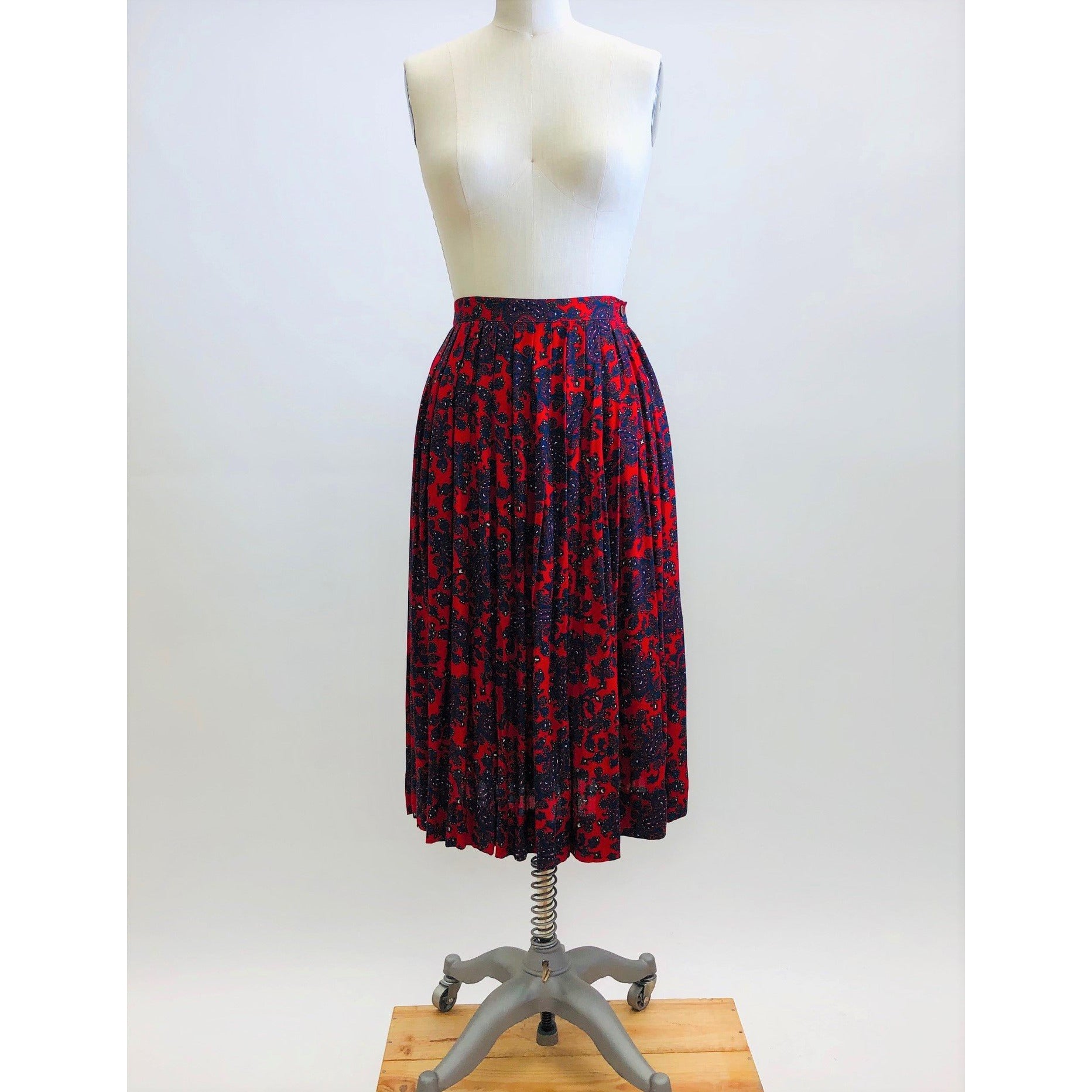 Feminine vintage red pleated skirt with a blue and purple paisley design. Midi length with side zipper closure. Beautiful vintage ribbon on inside hem finishing. A lovely piece for in-between seasons.