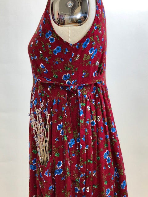 Burgundy sleeveless prairie dress with little blue and white flowers, gathered high doll waist and patch pockets to hold your freshly-picked flowers. Loose fit with double ties at waist to adjust for contouring. Midi length. This adorable dress looks homemade. 