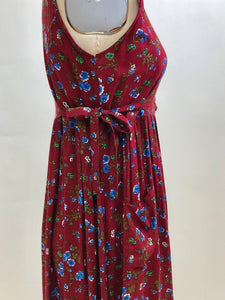 Burgundy sleeveless prairie dress with little blue and white flowers, gathered high doll waist and patch pockets to hold your freshly-picked flowers. Loose fit with double ties at waist to adjust for contouring. Midi length. This adorable dress looks homemade. 