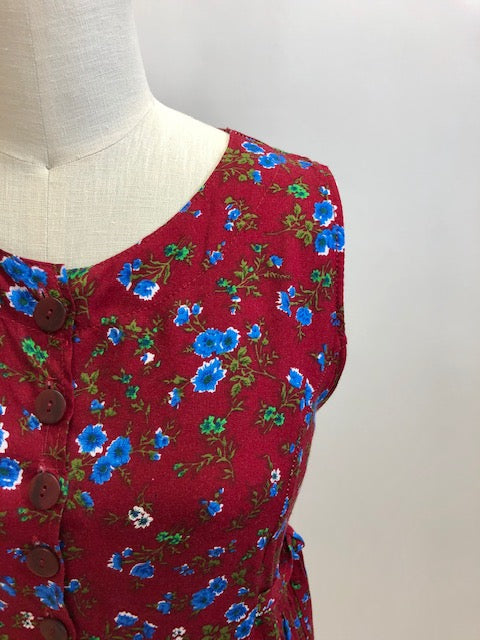 Burgundy sleeveless prairie dress with little blue and white flowers, gathered high doll waist and patch pockets to hold your freshly-picked flowers. Loose fit with double ties at waist to adjust for contouring. Midi length. This adorable dress looks homemade. 