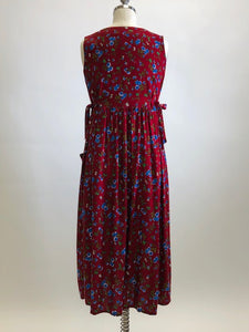 Burgundy sleeveless prairie dress with little blue and white flowers, gathered high doll waist and patch pockets to hold your freshly-picked flowers. Loose fit with double ties at waist to adjust for contouring. Midi length. This adorable dress looks homemade. 