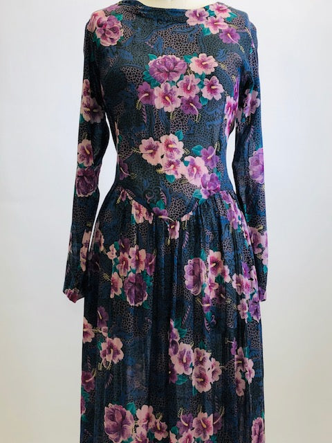 Gorgeous, airy long sleeve dress in purple and blue florals. This is made of a lightweight, sheer fabric so you will want to wear a light slip underneath. It features a v-shaped waistline with gathered skirt, and side seam pockets. The waist can be adjusted with waist ties at back. Button opening at back of bodice with a slight boat neck style. 