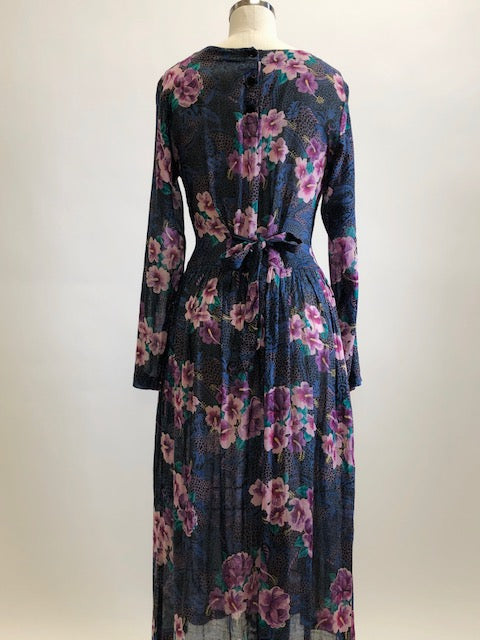 Gorgeous, airy long sleeve dress in purple and blue florals. This is made of a lightweight, sheer fabric so you will want to wear a light slip underneath. It features a v-shaped waistline with gathered skirt, and side seam pockets. The waist can be adjusted with waist ties at back. Button opening at back of bodice with a slight boat neck style. 