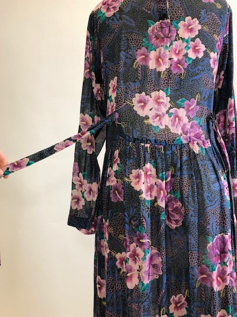 Gorgeous, airy long sleeve dress in purple and blue florals. This is made of a lightweight, sheer fabric so you will want to wear a light slip underneath. It features a v-shaped waistline with gathered skirt, and side seam pockets. The waist can be adjusted with waist ties at back. Button opening at back of bodice with a slight boat neck style. 