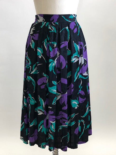 Stunning vintage midi flared skirt with waist pleats, side pockets and center back zipper. Black with purple and green floral print. Gorgeous silky viscose fabric with a sheen pattern. Perfect for dancing, twirling, and loving. Daniel Richie label. 