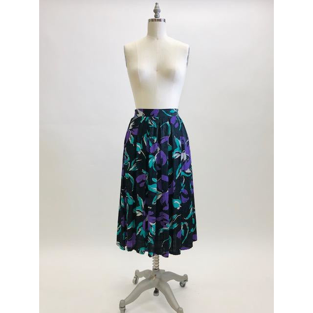 Stunning vintage midi flared skirt with waist pleats, side pockets and center back zipper. Black with purple and green floral print. Gorgeous silky viscose fabric with a sheen pattern. Perfect for dancing, twirling, and loving. Daniel Richie label. 