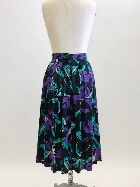 Stunning vintage midi flared skirt with waist pleats, side pockets and center back zipper. Black with purple and green floral print. Gorgeous silky viscose fabric with a sheen pattern. Perfect for dancing, twirling, and loving. Daniel Richie label. 