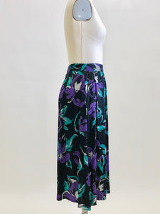 Stunning vintage midi flared skirt with waist pleats, side pockets and center back zipper. Black with purple and green floral print. Gorgeous silky viscose fabric with a sheen pattern. Perfect for dancing, twirling, and loving. Daniel Richie label. 