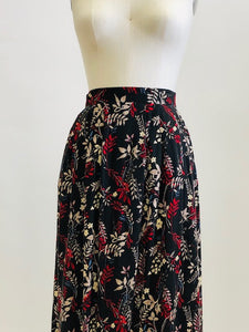 Vintage rayon maxi skirt with pleats at waistband featuring red, taupe and beige foliage and floral print against black background. Side seam pockets, and elasticated waistband in the back. Beautiful as an in-between seasons skirt and for a fall walk with tights and little boots.