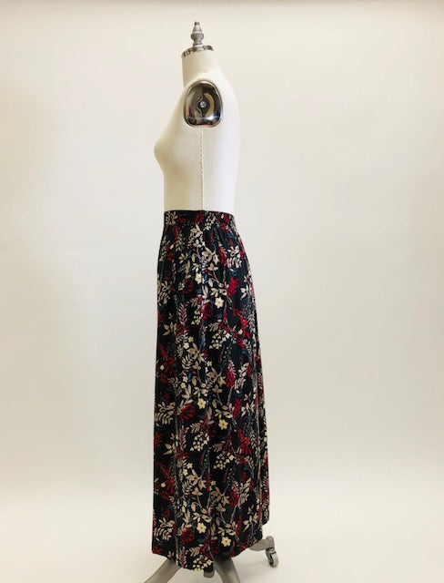 Vintage rayon maxi skirt with pleats at waistband featuring red, taupe and beige foliage and floral print against black background. Side seam pockets, and elasticated waistband in the back. Beautiful as an in-between seasons skirt and for a fall walk with tights and little boots.