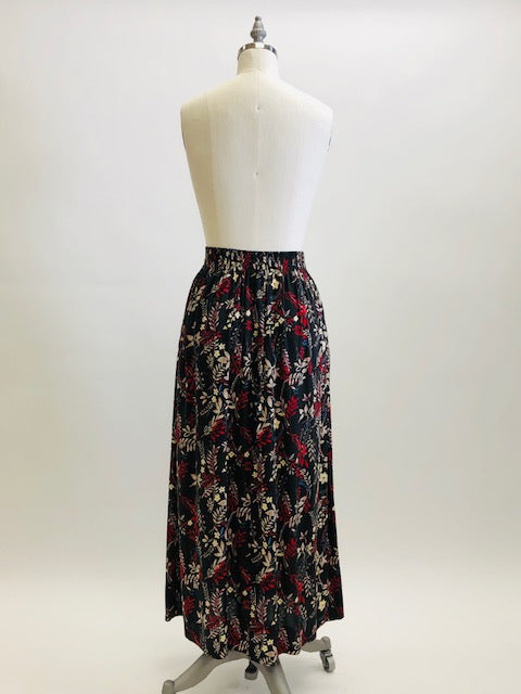 Vintage rayon maxi skirt with pleats at waistband featuring red, taupe and beige foliage and floral print against black background. Side seam pockets, and elasticated waistband in the back. Beautiful as an in-between seasons skirt and for a fall walk with tights and little boots.