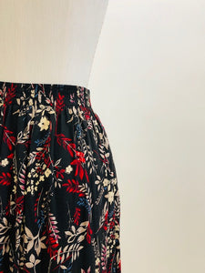 Vintage rayon maxi skirt with pleats at waistband featuring red, taupe and beige foliage and floral print against black background. Side seam pockets, and elasticated waistband in the back. Beautiful as an in-between seasons skirt and for a fall walk with tights and little boots.