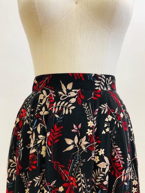 Vintage rayon maxi skirt with pleats at waistband featuring red, taupe and beige foliage and floral print against black background. Side seam pockets, and elasticated waistband in the back. Beautiful as an in-between seasons skirt and for a fall walk with tights and little boots.