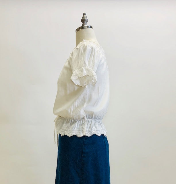 Adorable soft off-white top in a cotton/silk blend with elasticated peplum waist and neckline. This top features feminine eyelet detailing along the neckline, sleeve and waist hem, and pairs nicely with high waisted trousers, or a romantic linen skirt.