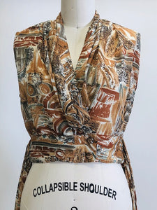 Vintage 90s short-waisted sleeveless wrap tie blouse with crossover button enclosure. Fabric pattern looks like European architectural shapes in brown tones. This top pairs nicely with high-waisted shorts or pants.