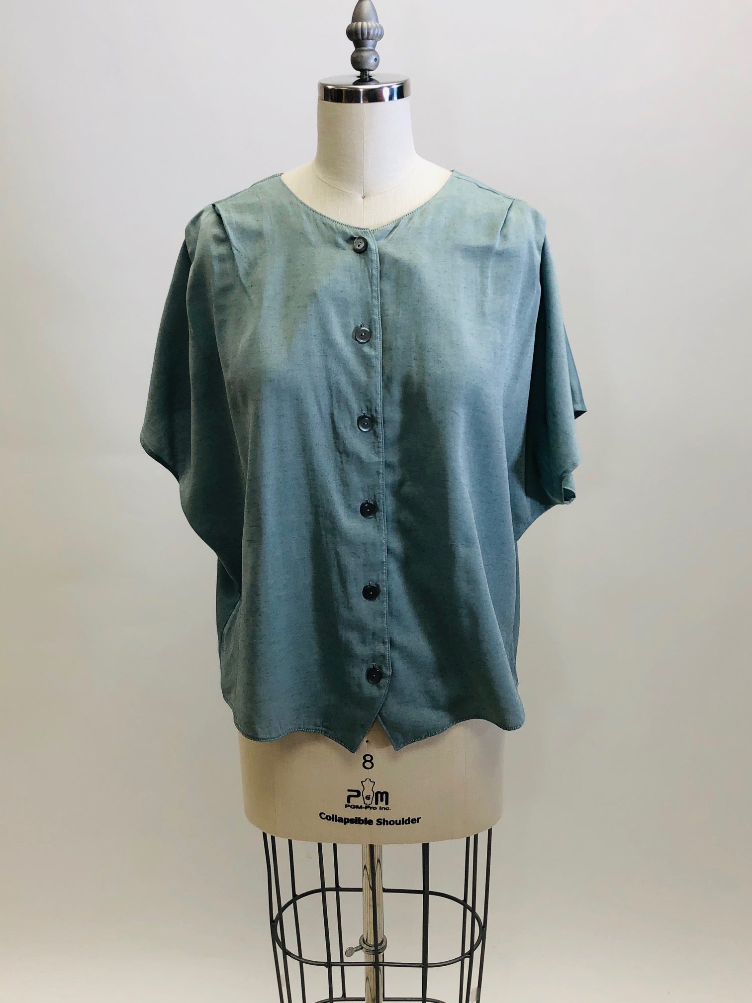 Vintage loose-fitting box shape top with button-down front, short kimono sleeve with interesting shoulder pleat detail. Sage green fabric with slight sheen. Worn like a one-size fits all style; great for tucking into linen trousers or shorts. 