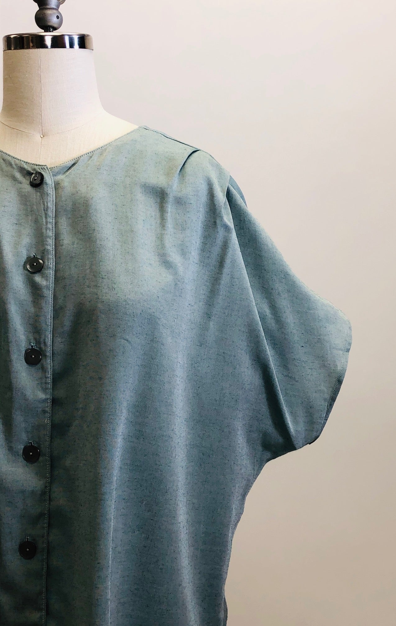 Vintage loose-fitting box shape top with button-down front, short kimono sleeve with interesting shoulder pleat detail. Sage green fabric with slight sheen. Worn like a one-size fits all style; great for tucking into linen trousers or shorts. 